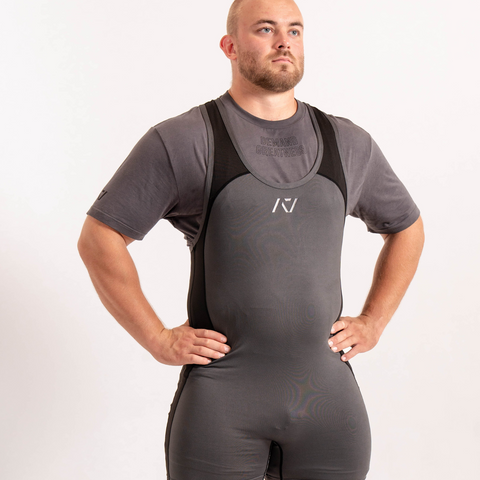 Front view of man wearing grey PF approved Shadow Stone Grey singlet and A7 Meet t-shirt in grey. Grey A7 logo on grey material with black straps and side panels. The grey A7 powerlifting singlet is made with premium materials and flatlock seams for maximum comfort on competition platform. 
