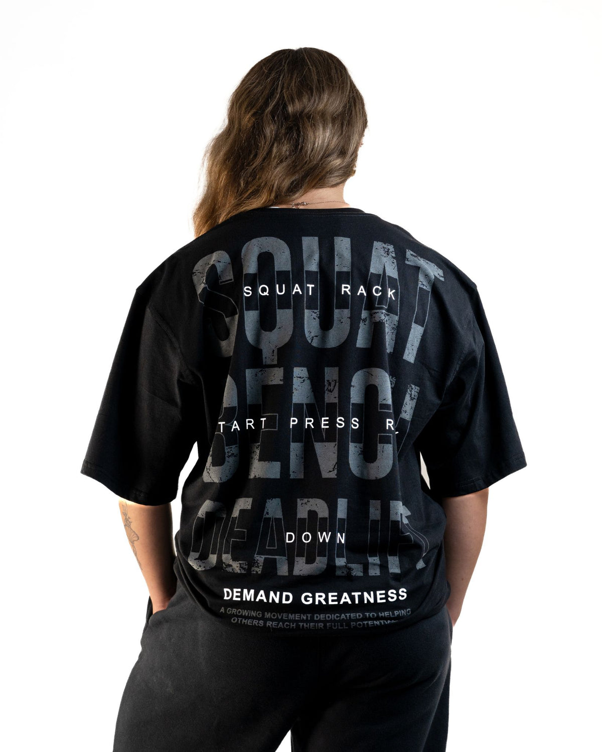 Back of the A7 Commands Overfit T-Shirt in black, showing Squat, Bench and Deadlift Commands. Worn by a women and unisex sizing, this strength sports apparel is gym wear apparel for travelling to meets and standing on the podium 