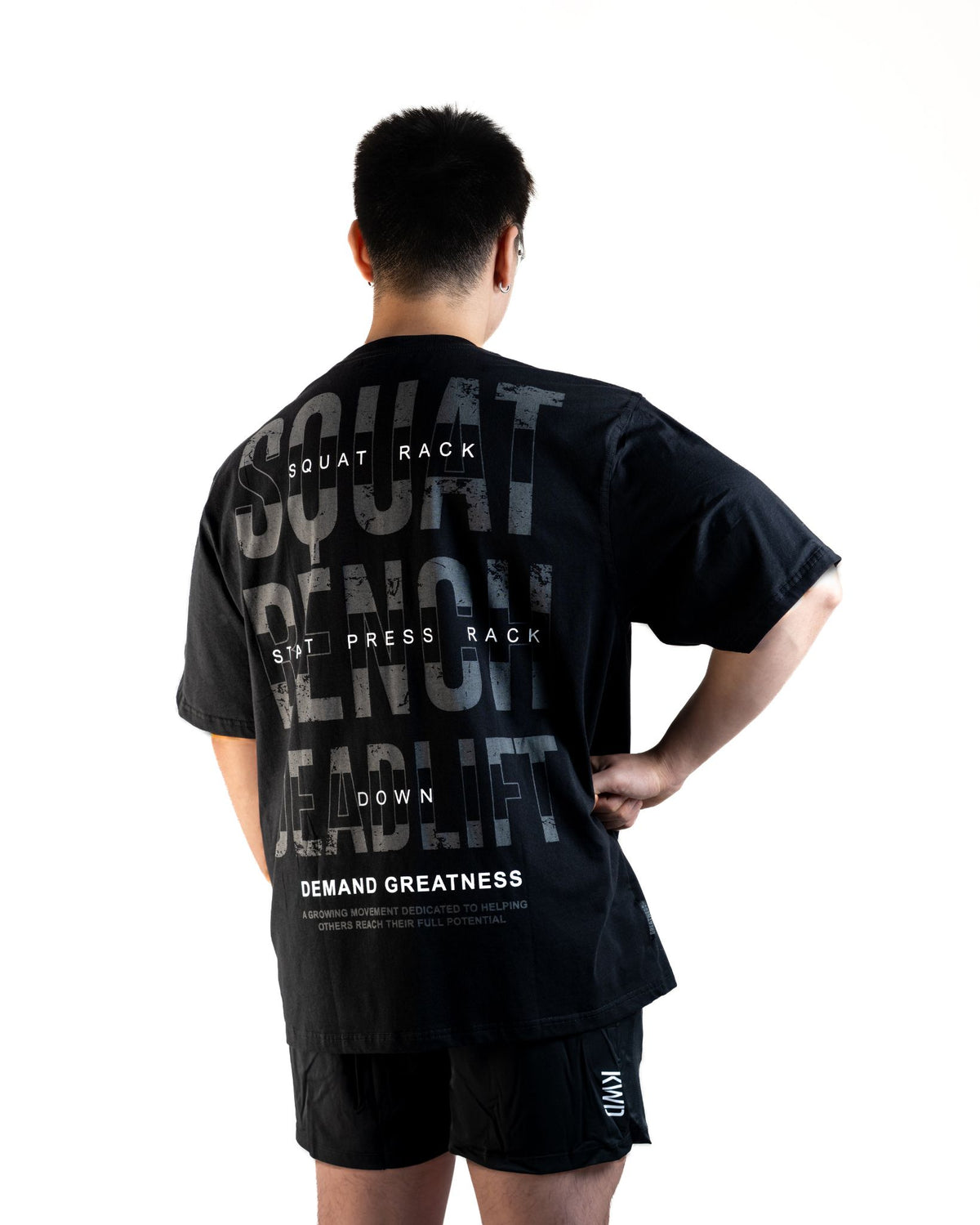 Back of the A7 Commands Overfit T-Shirt in black, showing Squat, Bench and Deadlift Commands. Worn by a man and unisex sizing, this strength sports apparel is gym wear apparel for travelling to meets and standing on the podium 