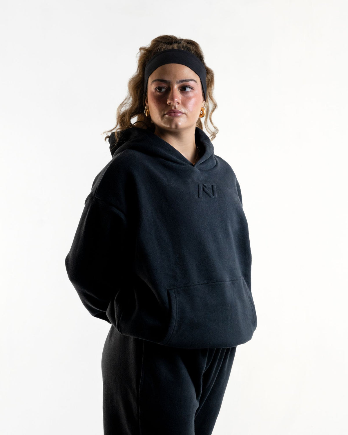 Front of the A7 Veil overfit hoodie in stealth/black. Worn by a woman and unisex sizing, this strength sports apparel is meet day apparel for traveling to meets and standing on the podium 