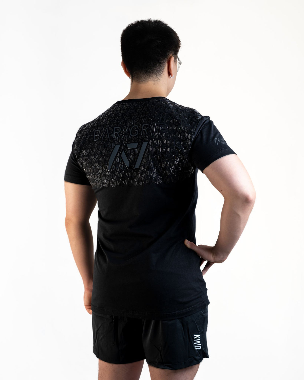 Back View Man wearing A7's Bar Grip COMMANDS shirt. Back view showing the A7 Bar Grip used for squatting and benching in commercial gyms without chalk. Paired with black KWD 360 GO shorts made from a stretchy squat proof material to use in powerlifting training
