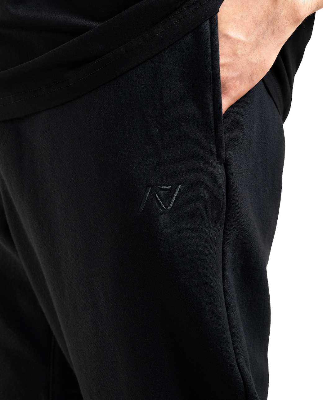 
Close up view of the A7 Veil overfit joggers and logo in stealth/black. Worn by a man and unisex sizing, this strength sports apparel is meet day apparel for traveling to meets and standing on the podium 