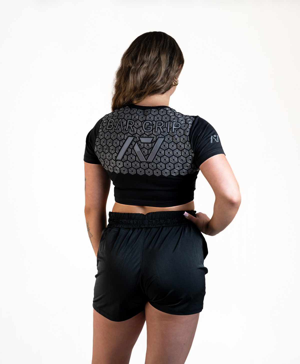 Back View Woman wearing A7's Bar Grip High Standards Low Bar Black shirt. Back view showing the A7 Bar Grip used for squatting and benching in commercial gyms without chalk. Paired with black KWD 360 GO shorts made from a stretchy squat proof material to use in powerlifting training