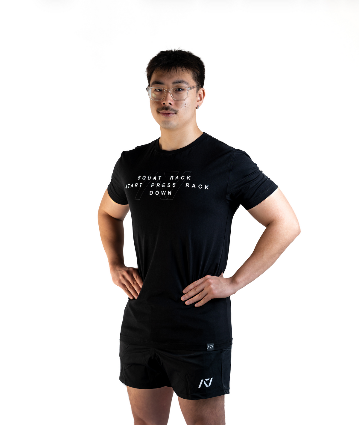 Front View of Man wearing A7's Bar Grip COMMANDS shirt. The Powerlifting Commands for Squat, Bench and Deadlift, written on the front in white and A7 logo outlined behind. Paired with black KWD 360 GO shorts made from a stretchy squat proof material to use in powerlifting training